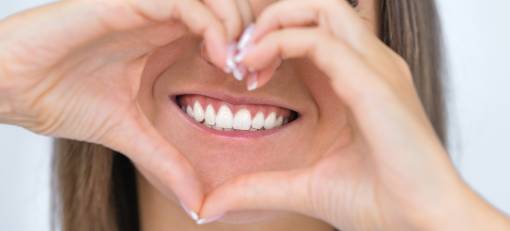 Woman with perfect smile makes a heart shape with her hand